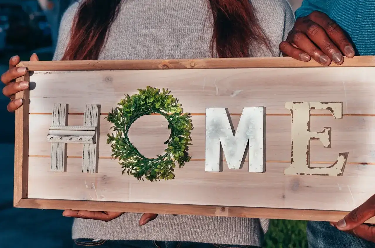 Dos personas sostienen un cartel que dice "HOME" con letras hechas en distintos materiales