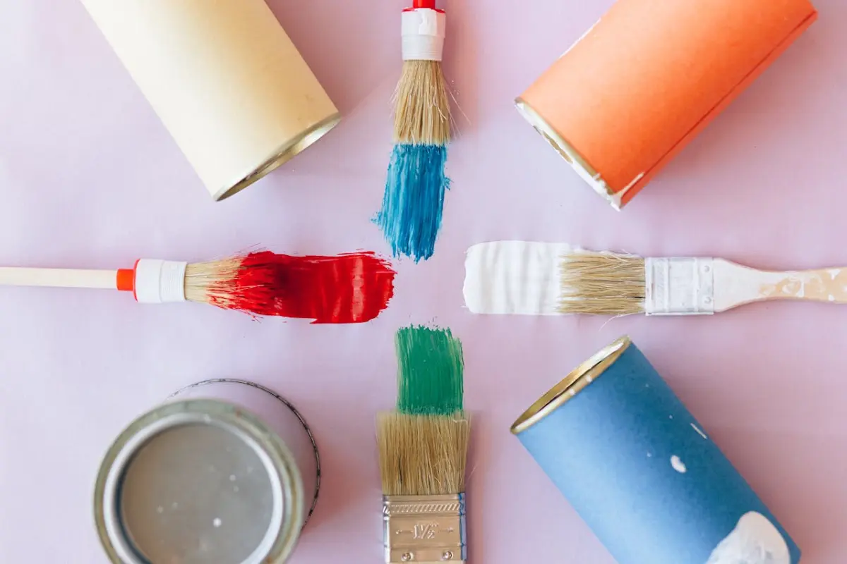 cuatro tarros de pintura, cuatro brochas sobre un fondo rosa claro