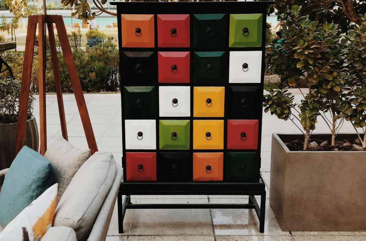 mueble con múltiples cajones pintados de colores. Se ven algunas platas y otros muebles