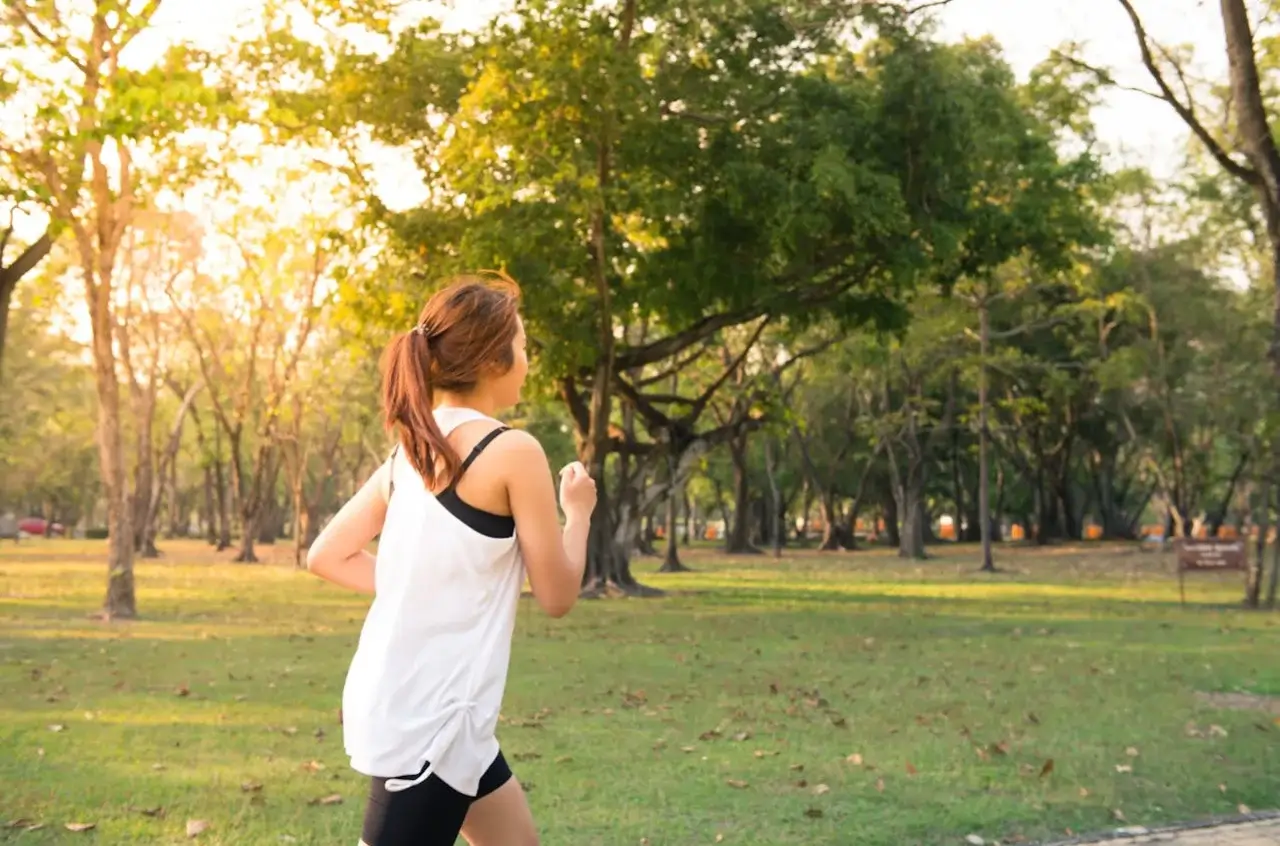 Mujer corriendo en un parque donde se ven algunos árboles y está cayendo el sol