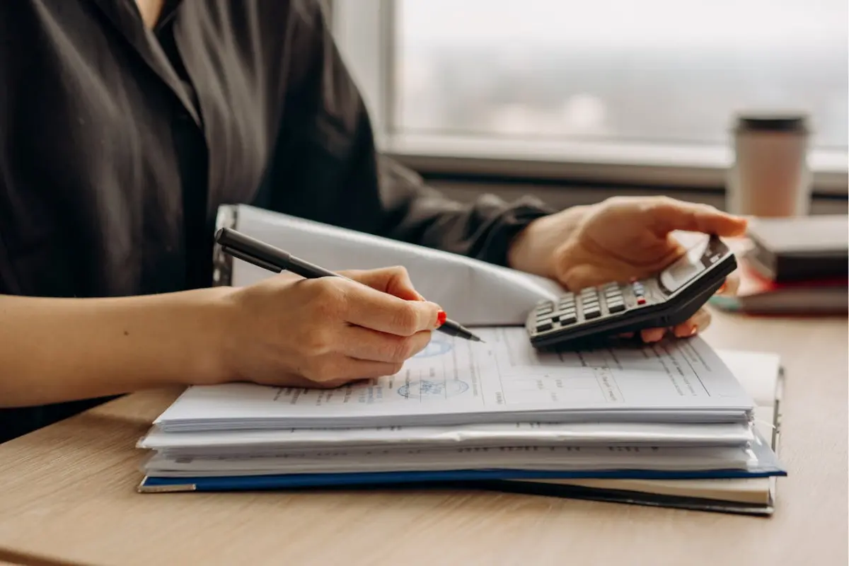 manos de una persona usando una calculadora mientras escribe en un cuaderno