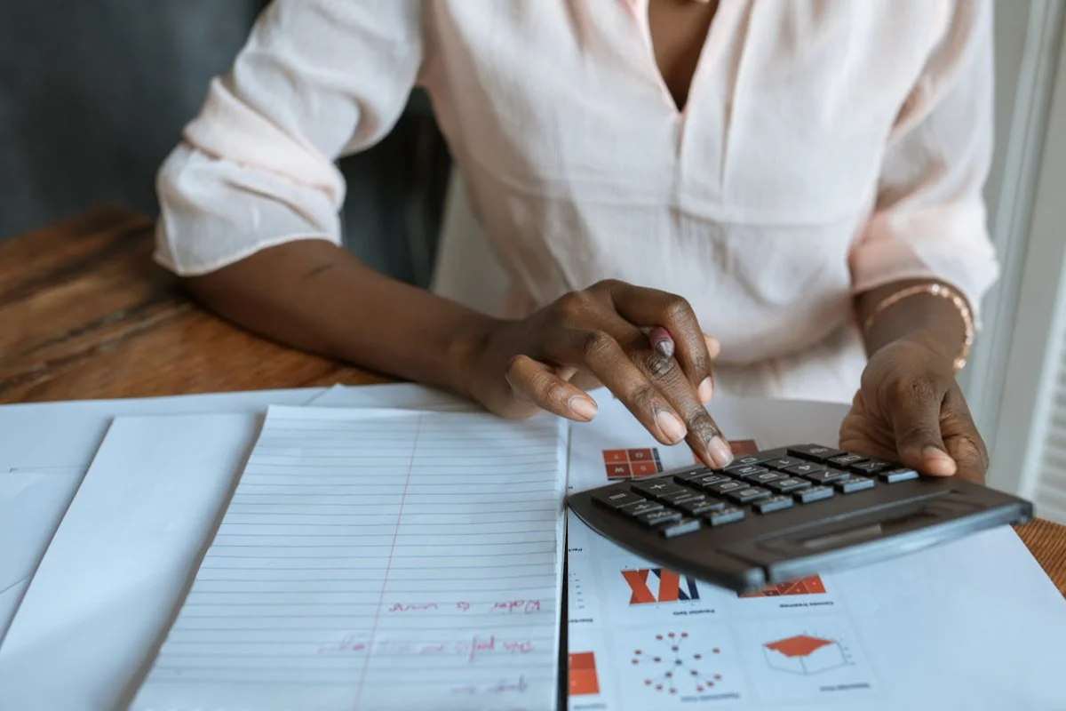 se ven las manos de una mujer usando una calculadora y unos documentos sobre la mesa