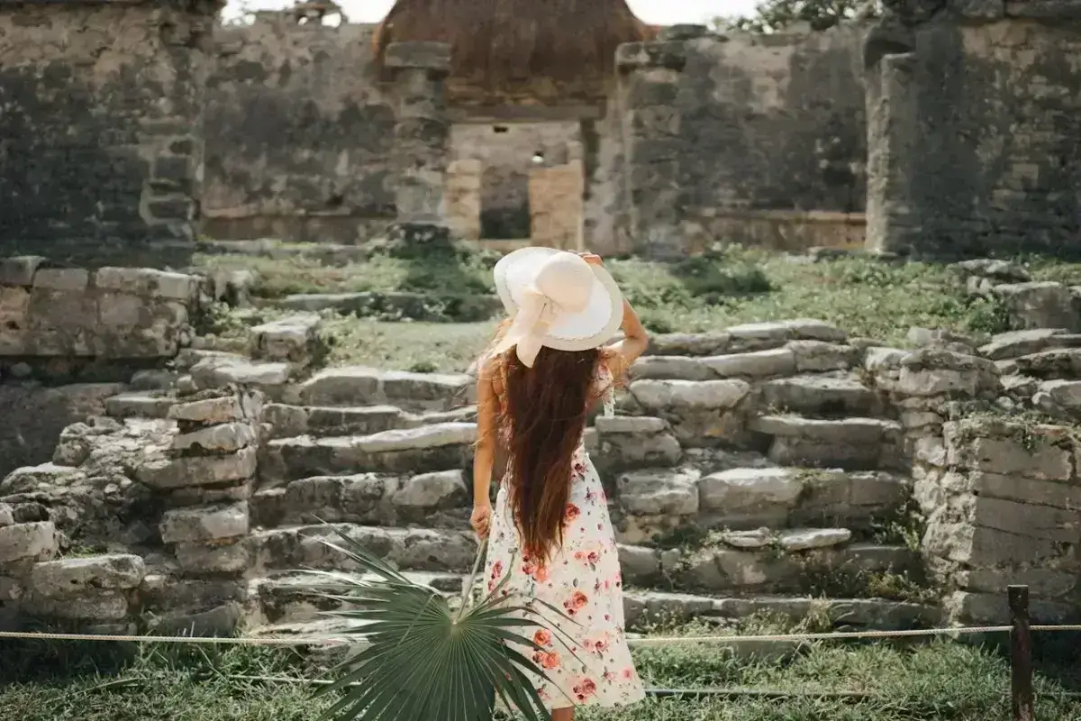 mujer jóven con vestido y sombrero observa unas escaleras y estructuras antiguas