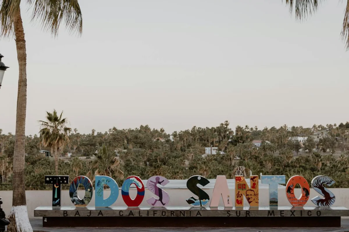 Letras en 3D que dicen "Todos los Santos" se ve vegetaciíin y un par de palmeras