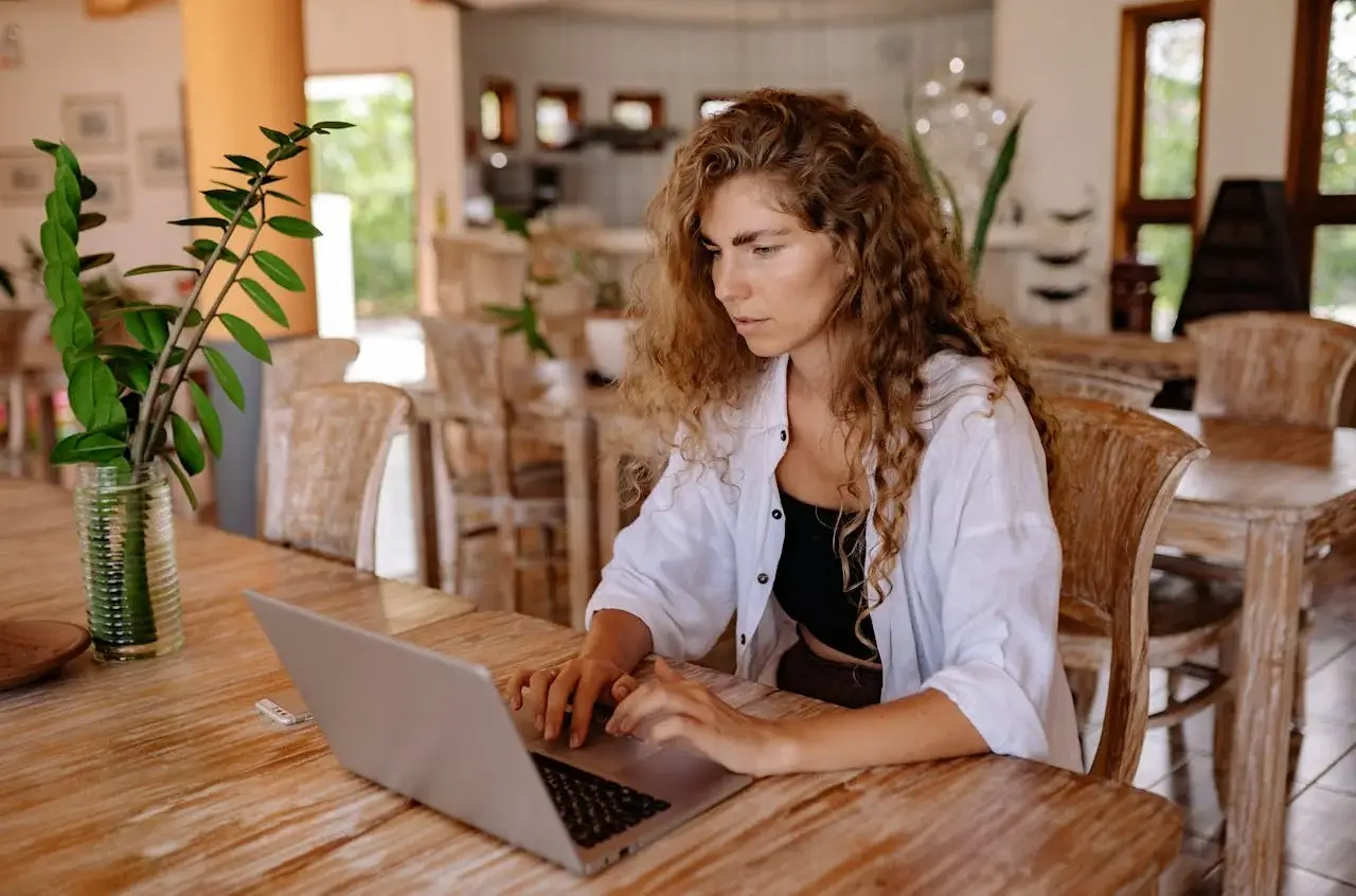 Mujer con una laptop haciendo una búsqueda, está en un lugar de una casa, en una mesa de madera