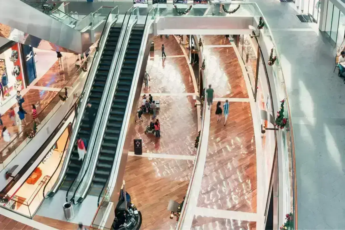 Vista desde arriba de un centro comercial en su interior. Se ven personas y unas escaleras eléctricas