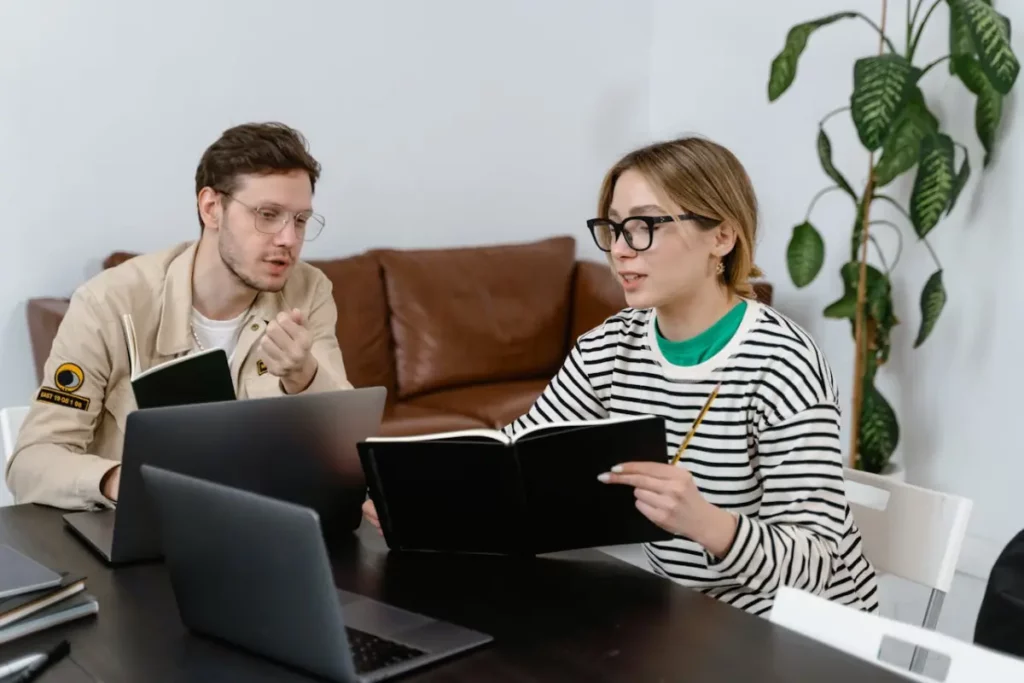 Un hombre y una mujer revisan anotaciones en una libreta, tienen sus laptops sobre el escritorio