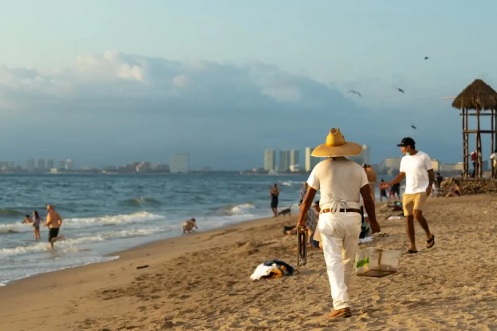 Playa donde se ve un vendedor y otras personas caminando o en el mar