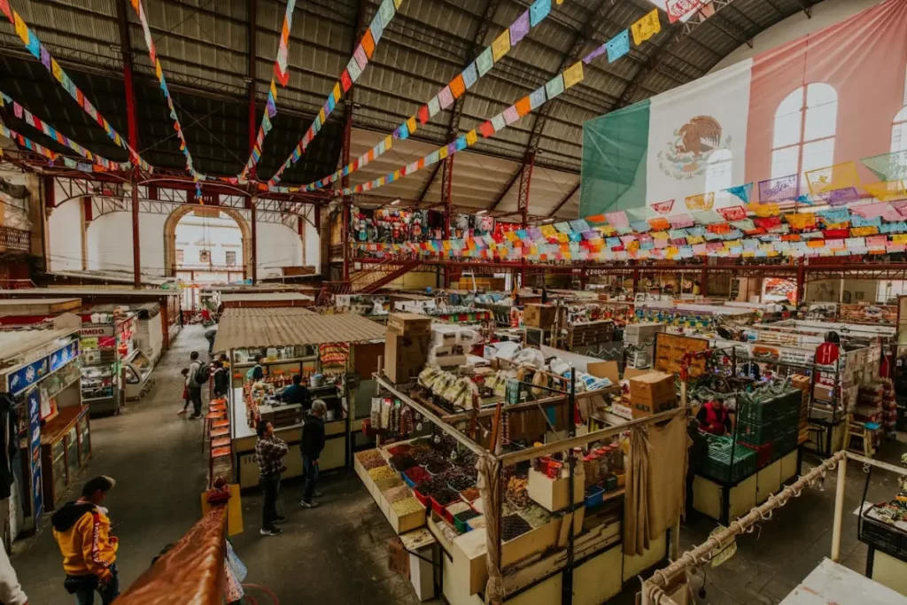 plaza de mercado con varias personas, una bandera de México colgada y decoraciones